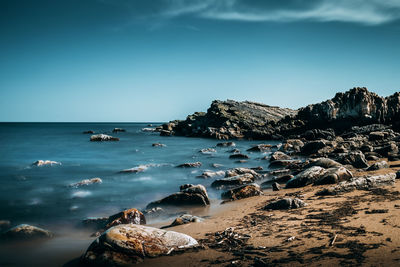 Rock formations at shore against clear blue sky