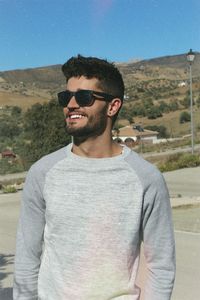 Smiling young man wearing sunglasses while standing against mountain