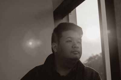 Portrait of young man looking through window at home