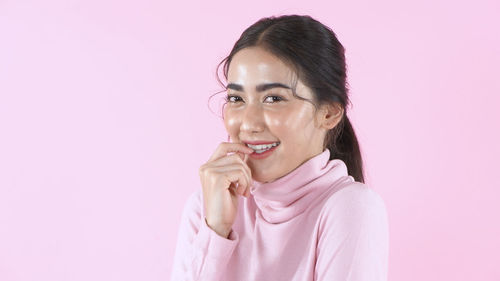 Portrait of smiling young woman against pink background