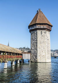 Old building by river against clear blue sky