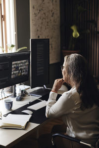 Female freelancer with hand on chin during video conference through computer at home office