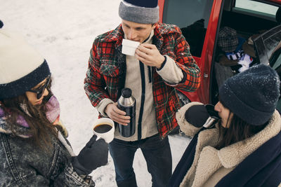 High angle view of friends having coffee while talking by car on snow