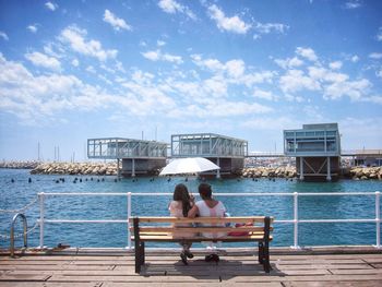 Rear view of couple sitting on bench against sky