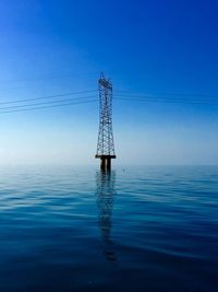 Electricity pylon by sea against blue sky