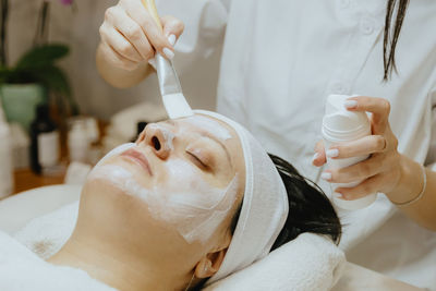 A girl cosmetologist applies a cream mask to a woman s face with a brush.