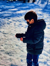Side view of boy wearing mask standing on snow covered land