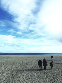 Rear view of people standing on beach against sky