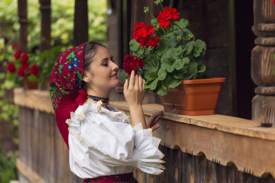 Beautiful young woman in romanian clothing smelling flowers at yard