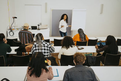 Smiling professor teaching students while standing by flipchart in classroom