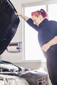 Female mechanic opening car's hood in auto repair shop