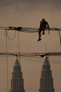 Low angle view of man working on rope against sky during sunset