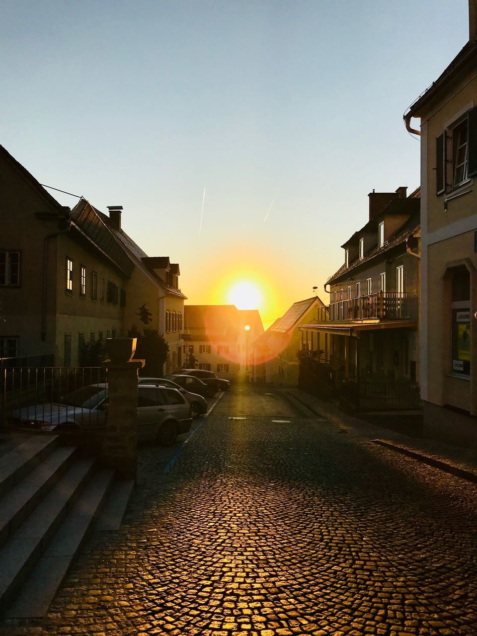 building exterior, architecture, built structure, sunset, sun, cobblestone, sunlight, sky, outdoors, residential building, clear sky, no people, city, day