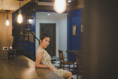 Portrait of young woman by table at restaurant