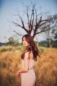 Young woman standing on field against sky