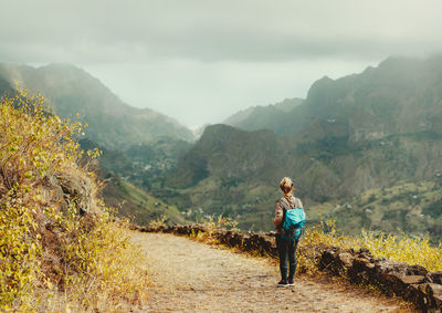 Rear view of woman standing on land against mountains and sky