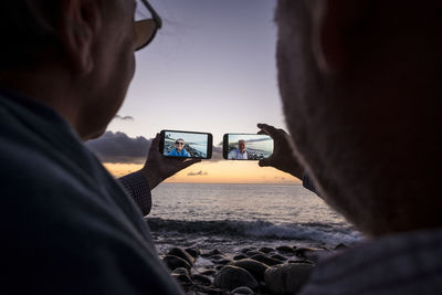 Couple taking selfie from mobile phones at beach during sunset