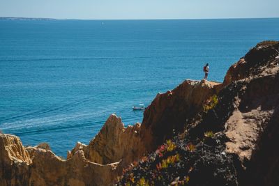 Man standing on cliff by sea against clear sky