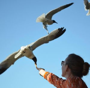 Low angle view of woman flying against clear blue sky