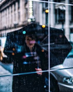 Woman with umbrella standing in rain seen from wet window