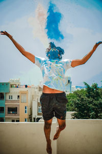 Rear view of man with arms outstretched standing against wall