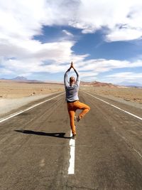 Rear view of mid adult man practicing tree pose on road against sky