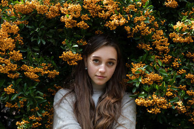 Close-up portrait of young woman standing against orange berries on plant