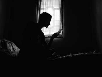 Low angle view of woman using mobile phone while sitting on bed in darkroom