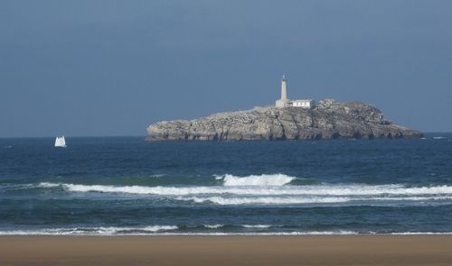 Lighthouse by sea against clear sky