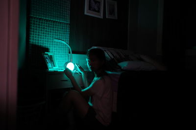 Side view of woman holding illuminated light on night table