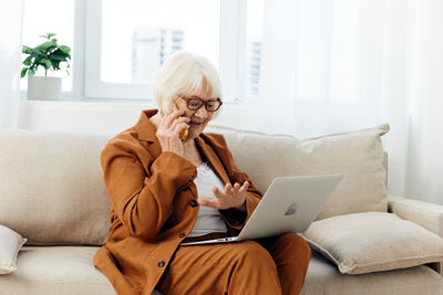 Young woman using laptop while sitting on sofa at home