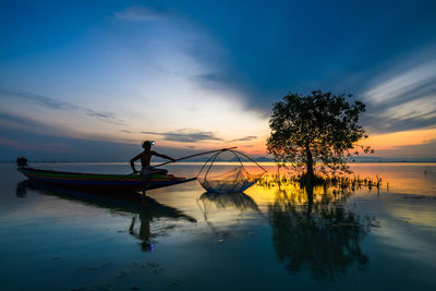 Silhouette man fishing in lake against sky during sunset