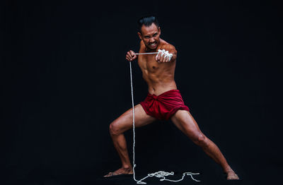 Portrait of shirtless mid adult man exercising with rope against black background