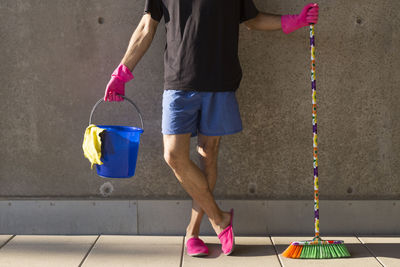 Low section of man with cleaning equipment standing against wall