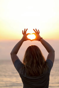 Rear view of woman making heart shape with sun in between