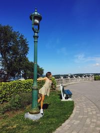 Woman standing on street light by footpath