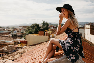 Side view of smiling young woman sitting on rooftop