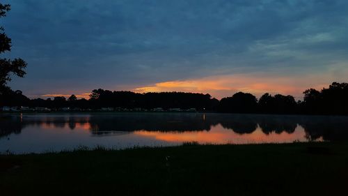 Reflection of trees in calm lake at sunset