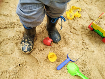 Child feet in small rubber boots stained in sand in a sandbox among toys