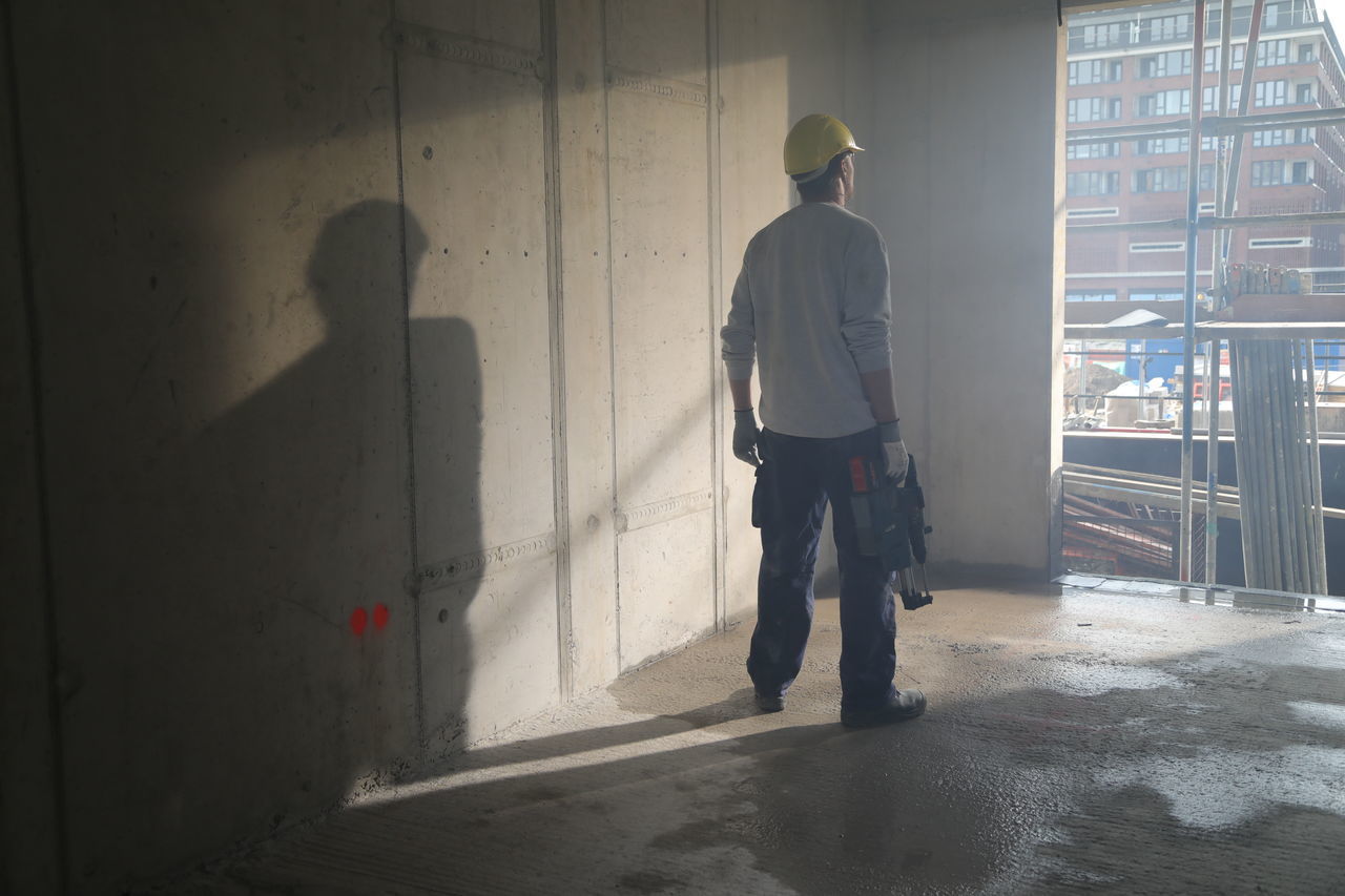 REAR VIEW OF MAN STANDING ON CONSTRUCTION SITE