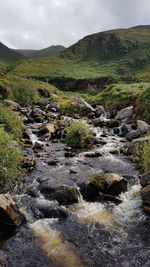 Scenic view of stream flowing through rocks against sky