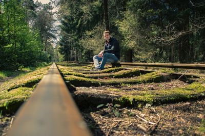 Low angle portrait of man sitting on abandoned railroad track