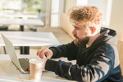 Side view of man using mobile phone while sitting on table