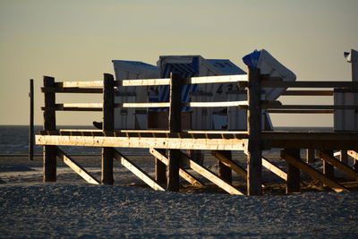 Hooded chairs on pier at beach against sky