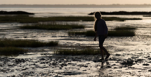 Rear view of man walking at beach during sunset