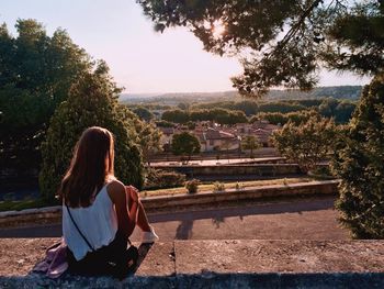 Rear view of woman sitting on wall during sunny day