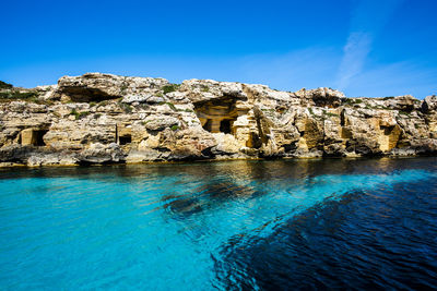 Rocks in sea against clear blue sky