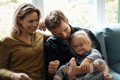 Happy parents sitting with cute daughter on sofa in living room at home