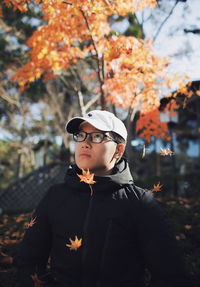 Young man looking away while standing on tree during autumn