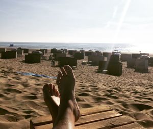 Low section of woman resting on beach against sky